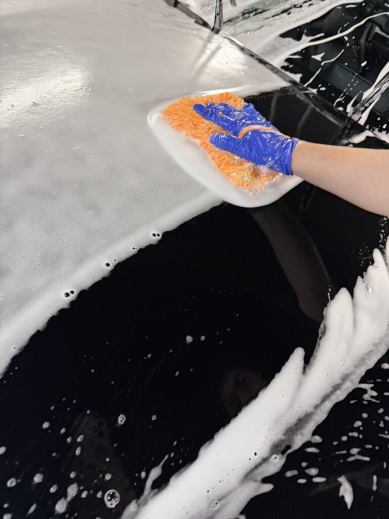実際に洗車を体験して撮影した、泡のついた黒い車をオレンジと青のグローブで手洗いしている様子